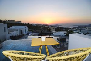 een gele tafel en stoelen op een balkon met uitzicht op de zonsondergang bij Nova Luxury Suites in Pirgos