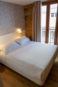 ein großes weißes Bett in einem Zimmer mit Fenster in der Unterkunft A Bughina apartamentos in Muxia