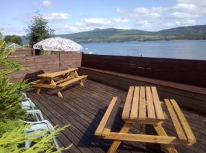 una terraza de madera con 2 mesas de picnic y una sombrilla en Maggie's en Inveraray