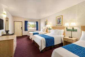 a hotel room with three beds and a flat screen tv at Travelodge by Wyndham Niagara Falls - New York in Niagara Falls
