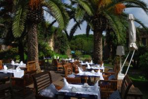 a restaurant with tables and chairs and palm trees at UNAHOTELS Club Hotel Ancora in Stintino
