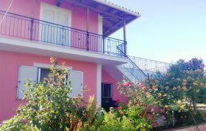 Casa de color rosa con balcón y algunos árboles en Paliorouga Lodge Zakynthos, en Langadhákia