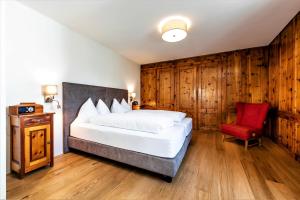 a bedroom with a bed and a red chair at Hotel Münsterhof in Müstair