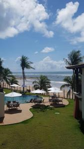 a pool with tables and umbrellas next to the beach at Bali Bahia Itacimirim in Itacimirim