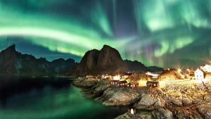 una isla en el agua bajo la aurora boreal en Eliassen Rorbuer, en Reine