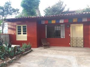 une maison rouge avec une chaise en face dans l'établissement "Chalé Balines Oroboro" 1 - Casa com jardim de 150 m e cozinha completa em Macacos, à Macacos