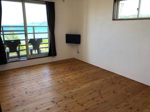 a room with a wooden floor and two windows at Guest room Halemakana in Amami