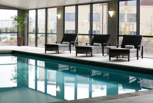 a pool with chairs and tables next to a building at Sudima Auckland Airport in Auckland