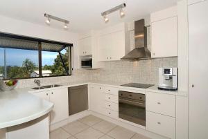 cocina con armarios blancos, fregadero y ventana en Commodore Apartments, en Noosa Heads