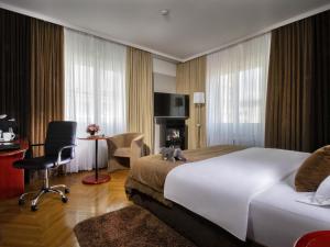 a hotel room with a bed, desk, chair and a lamp at Best Western Premier Hotel Slon in Ljubljana