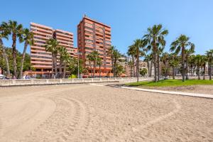 an empty beach with palm trees and a tall building at iloftmalaga Miramar in M&aacute;laga