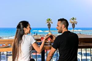 Ein Mann und eine Frau sitzen an einem Tisch am Strand in der Unterkunft Prima Tel Aviv Hotel in Tel Aviv