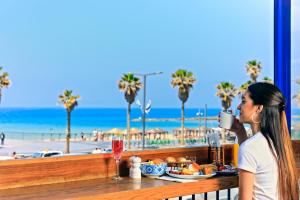 a woman sitting at a table with a drink and the beach at Prima Tel Aviv Hotel in Tel Aviv