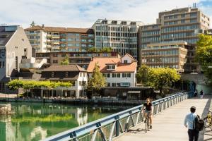 una coppia su un ponte sopra un fiume con edifici di EMA House Hotel Suites a Zurigo