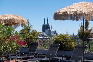 eine Gruppe von Stühlen und Sonnenschirmen mit Skyline der Stadt in der Unterkunft Mauritius Hotel & Therme in Köln