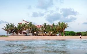 a man standing on the beach in front of a house at Cardamon Hotel Nilaveli in Nilaveli