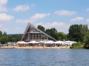 a building with tables and umbrellas next to a body of water at Ferienhaus Seerose in Hohenfelden