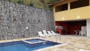einen Pool mit Stühlen und einer Steinmauer in der Unterkunft Aconchego da Serra in Teresópolis