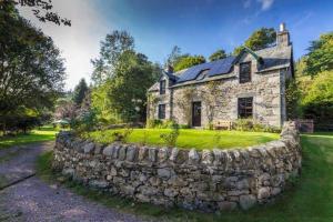 an old stone house with a stone wall at The Ferry House Cottage in Aberfeldy