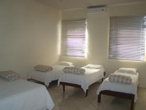 three beds in a room with white walls and windows at Pousada Quati in Foz do Iguaçu