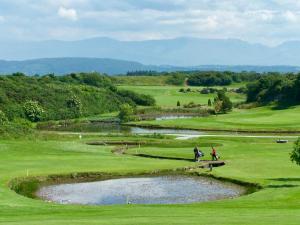 two people on a golf course with a pond at Bungalow33 Benllech in Benllech