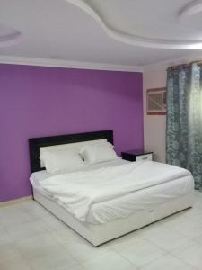 a bedroom with a white bed with a purple wall at Wahat Al Yarmouk Serviced Apartments in Ţubarjal