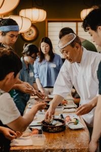 a chef preparing food on a table with a group of people at Emblem Hostel Nishiarai in Tokyo
