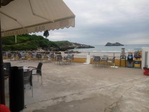 a beach with chairs and tables and the ocean at Pensión El Tabanu in Celorio