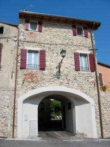 a stone building with an archway and red shutters at B&B Antiche Mura in Puegnano del Garda