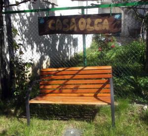 un banco de madera sentado en el césped bajo un cartel en Casa Olga, en Triacastela