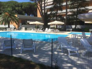 a swimming pool with white chairs and umbrellas at Residence il Pino in Marina di Castagneto Carducci