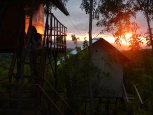 a woman sitting on the stairs of a house at sunset at Rumah Pohon in Nusa Penida