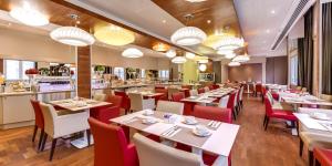 ナントにあるメルキュール ナント サントル グランド ホテルの白いテーブルと赤い椅子が備わるレストラン