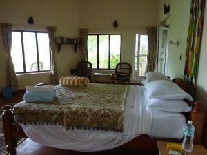 a bedroom with a large bed with white sheets and windows at Cardamom House in Sembatti