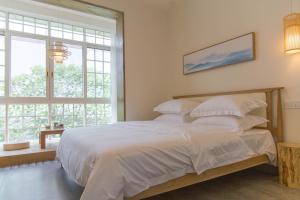 a bedroom with a bed with white sheets and a window at Bloom Time Guest House in Dujiangyan