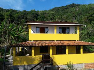 a yellow house with a mountain in the background at Suítes Encanto do Pai in Praia de Araçatiba