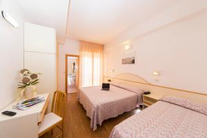 una camera d'albergo con 2 letti e una scrivania di Hotel Silvia a Misano Adriatico