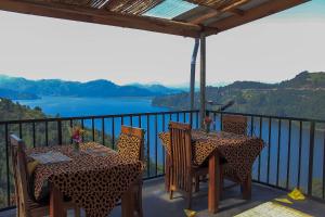 Lake Mulehe Gorilla Lodge في Kisoro: طاولتين وكراسي على شرفة مطلة على بحيرة