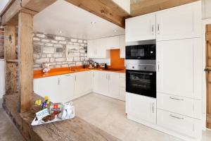a kitchen with white cabinets and a stone wall at The Old Dairy, Heritage Escapes, Field House Farm in Bempton