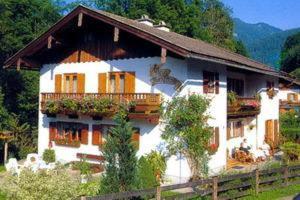 ein großes weißes Haus mit einem Zaun davor in der Unterkunft Alpenpension Auengrund in Ramsau bei Berchtesgaden