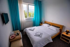 a bedroom with a bed with blue curtains and a window at Pensiune Perla - Bistrița Năsăud in Susenii Bîrgăului +149 photos