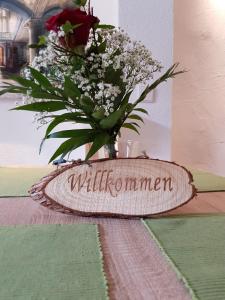 eine Vase voller Blumen auf einem Tisch mit einem Schild in der Unterkunft Lindes Ferienwohnung in Dinkelsbühl
