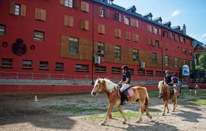 drie mensen die paardrijden voor een rood gebouw bij Hotel Hipic in Vielha