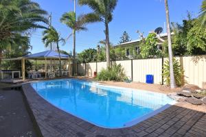 a swimming pool in a yard with a fence and palm trees at Alexandra Park Motor Inn in Bundaberg