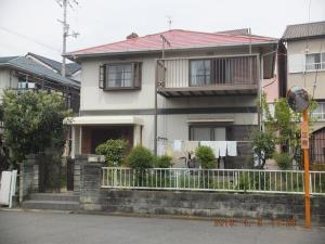 a white house with a fence in front of it at Hirakata-park Guesthouse in Hirakata