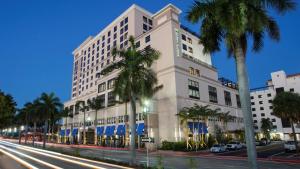 a large white building on a city street with palm trees at Hyatt Place Boca Raton in Boca Raton
