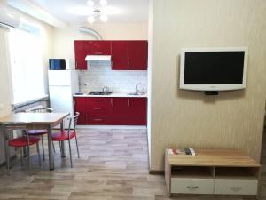 クラマトルスクにあるStusa 2 bedroom luxury apartmentのキッチン(赤いキャビネット、テーブル、壁掛けテレビ付)