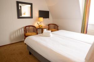 a bedroom with a large white bed and two chairs at Hotel Hof van Twente in Hengevelde