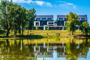 a building next to a lake with trees at Open Hotel Szentes in Szentes