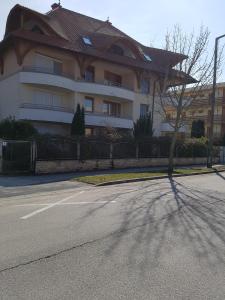 a building with a tree in front of a street at Napsugár Apartman in Balatonlelle